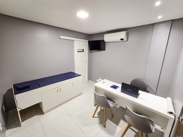 A mesma sala vista da porta, com a maca à esquerda e a mesa de atendimento à direita