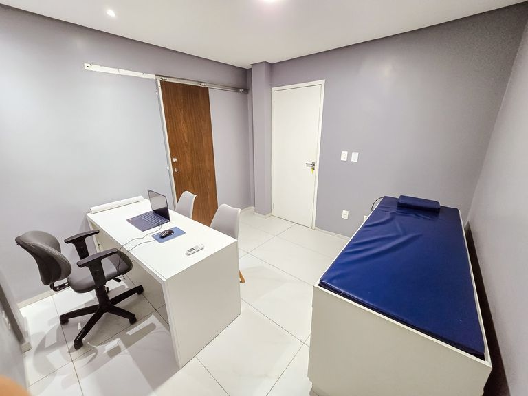 Sala de atendimento com mesa, duas cadeiras e maca de exame