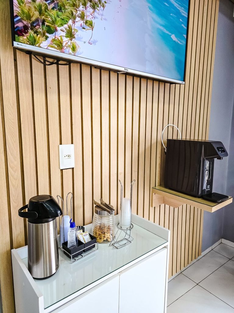 Cantinho do café na sala de espera, com garrafa térmica, copos e TV