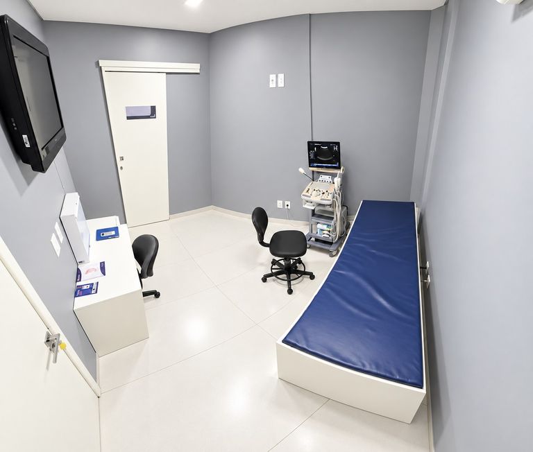 Terceira sala de atendimento, com maca, mesa de trabalho e monitor